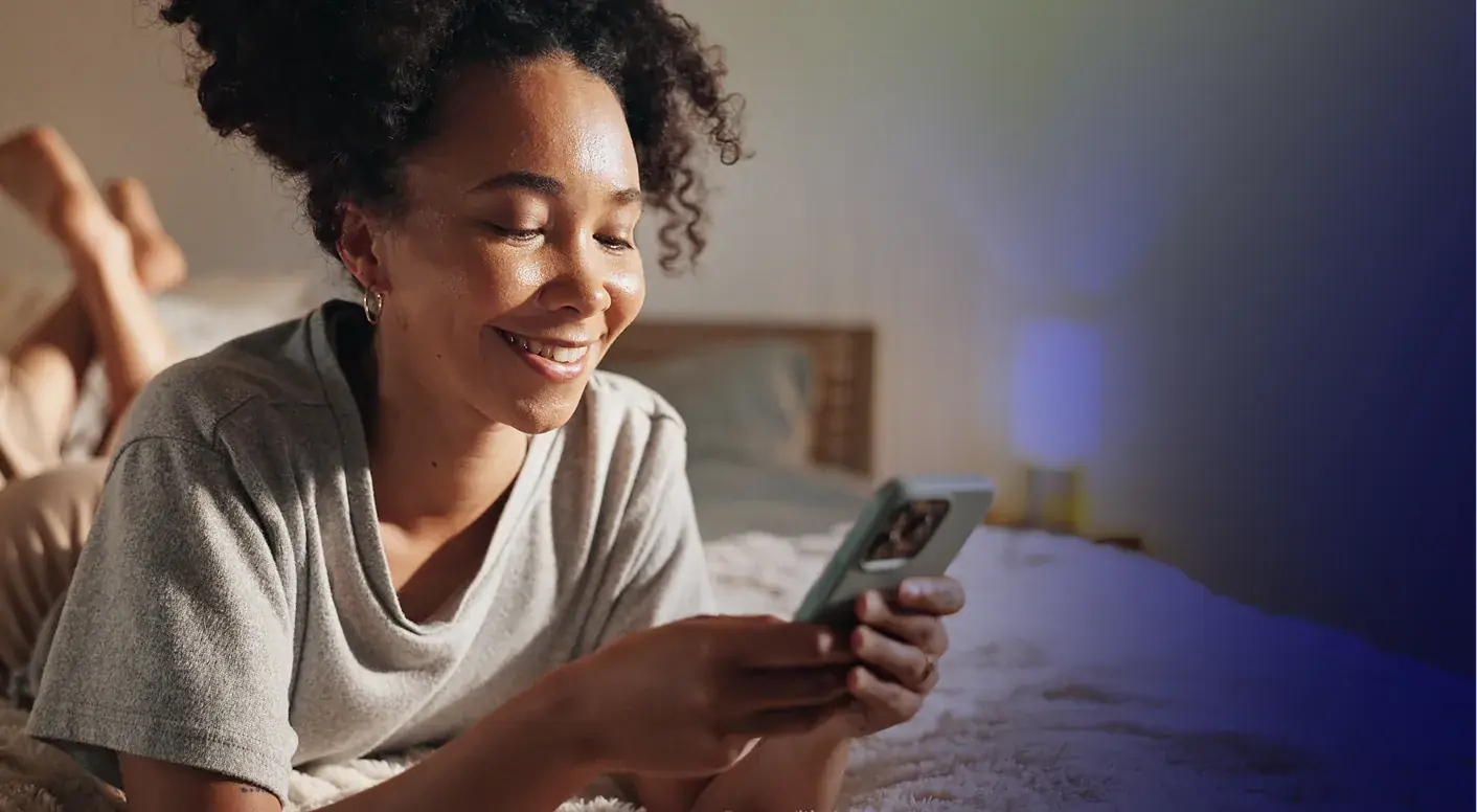 A woman smiling at her phone while lying in bed